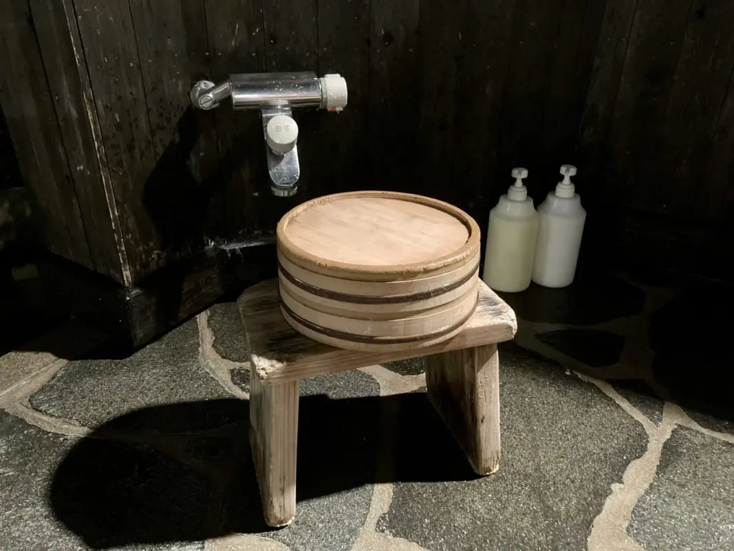 Traditional Japanese onsen washing area with a wooden stool, wooden bucket, and washing station used before entering the hot spring.