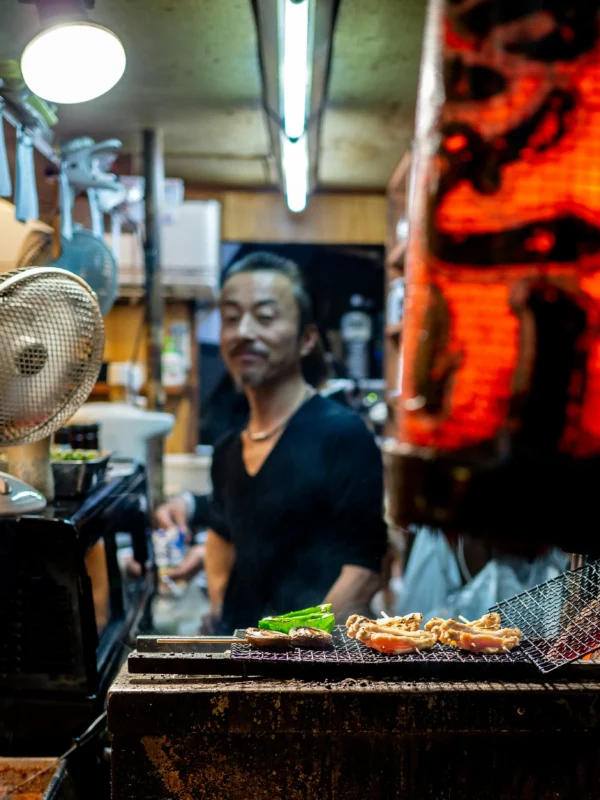yoav-aziz-BZ-abLvxmyQ-unsplash Yakitori being grilled at a Japanese izakaya counter with the chef in the background