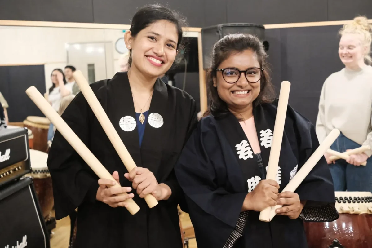 att.T8uNisexgnPjd-VHswyx4hCVaCtO1oO1tDcLCn7Zbw4 2 Travelers smiling with bachi during a private taiko drumming in Tokyo