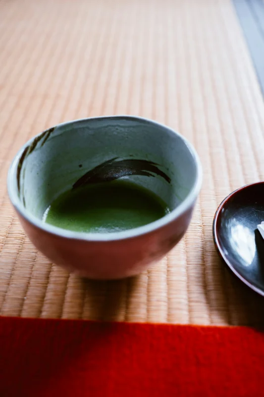pjh-SLgkv8j16Gk-unsplash Close-up of matcha tea in ceramic bowl on tatami mat during tea ceremony in Japan