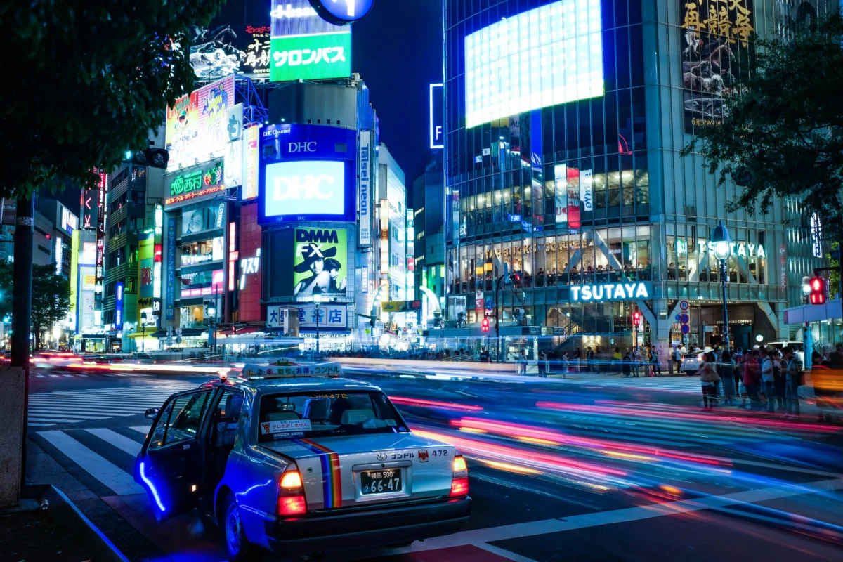 alex-knight-xX6BOQ0fJvk-unsplash Shibuya crossing at night with neon signs and a taxi in Tokyo