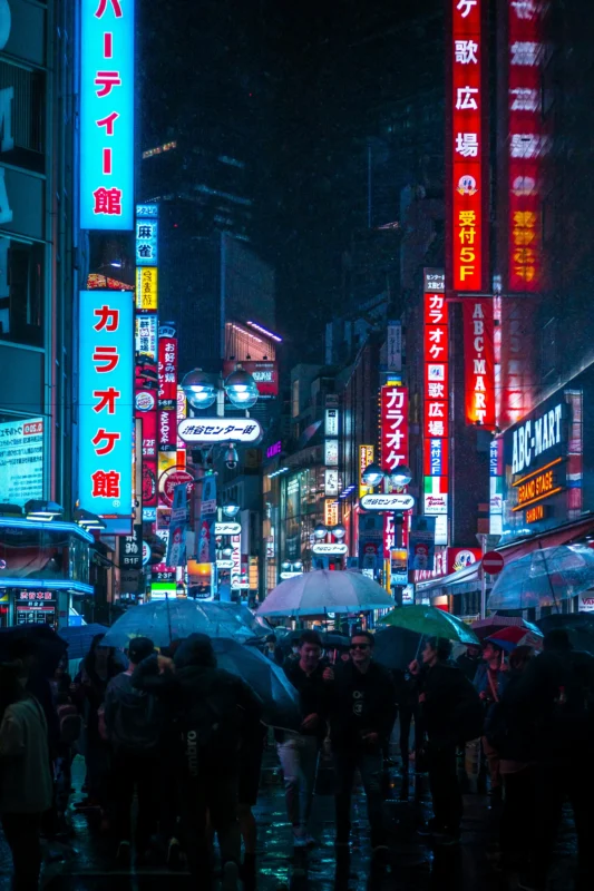 Crowded Shibuya Center-Gai at night with neon signs and people holding umbrellas